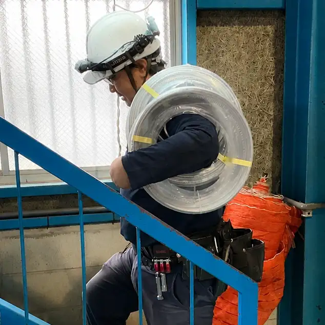 電線リールを担いで階段を移動する電気工事士