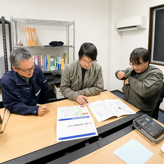 図面や技術資料を囲んで打ち合わせを行うスタッフ